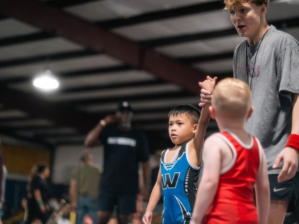 Referee raising the hand of a smiling young wrestler after a tournament win
